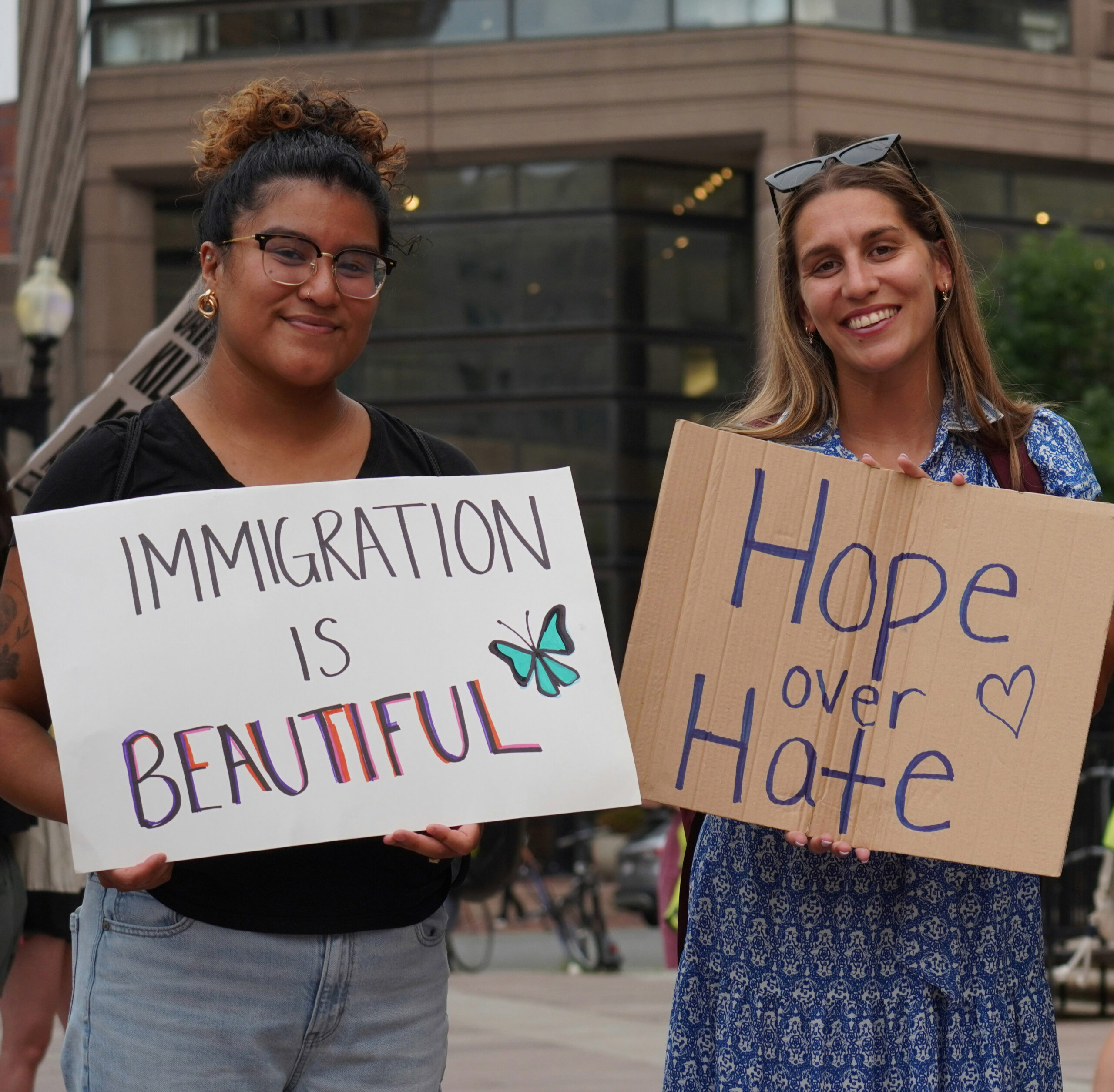 two women holding signs saying Immigration is Beautiful and Hope Over Hate